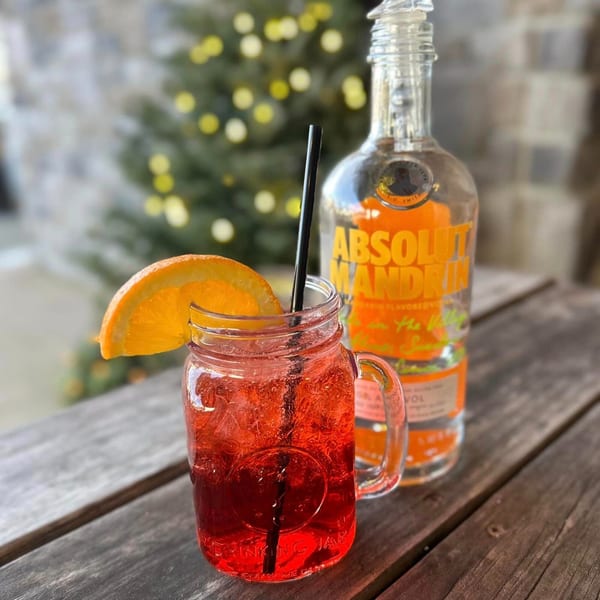 A red cocktail in a mason jar with an orange slice and straw, next to a bottle of Absolut Mandrin.
