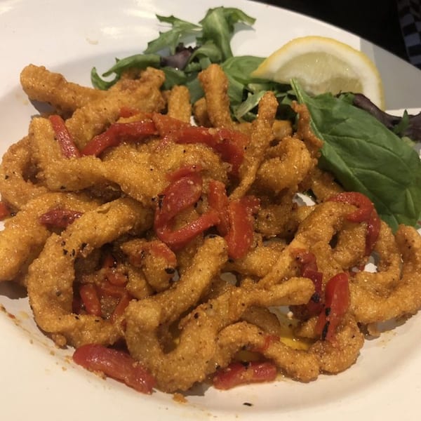 Crispy fried calamari with red peppers, a lemon wedge, and greens on a white plate.